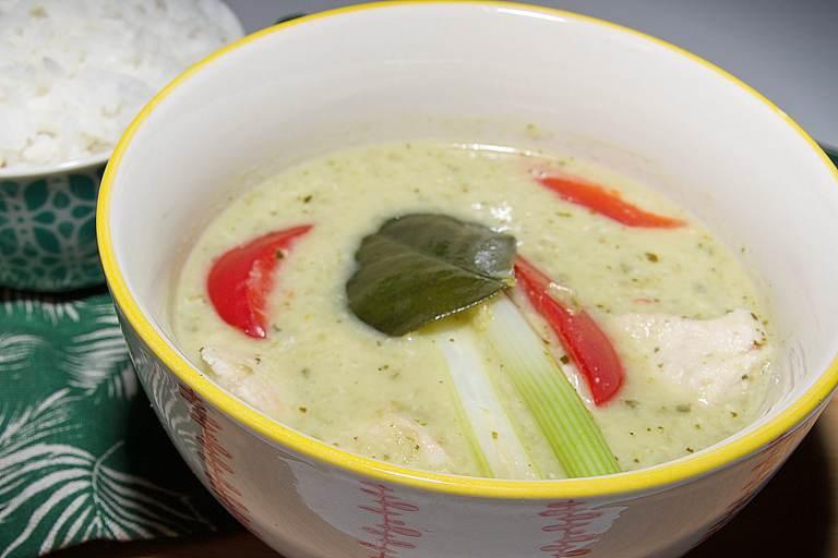 A traditional bowl of creamy, aromatic Thai green curry with chunks of chicken in a small bowl with jasmine rice.
